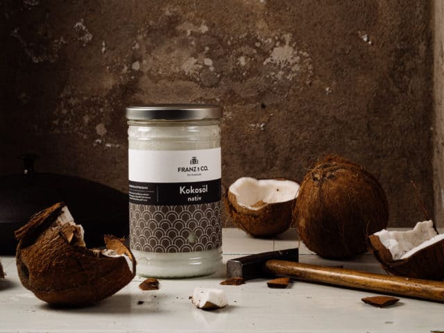 950 ml Glas FRANZ & CO. Kokosöl nativ mit Hammer und aufgeschlagenen Kokosnüssen drum herum